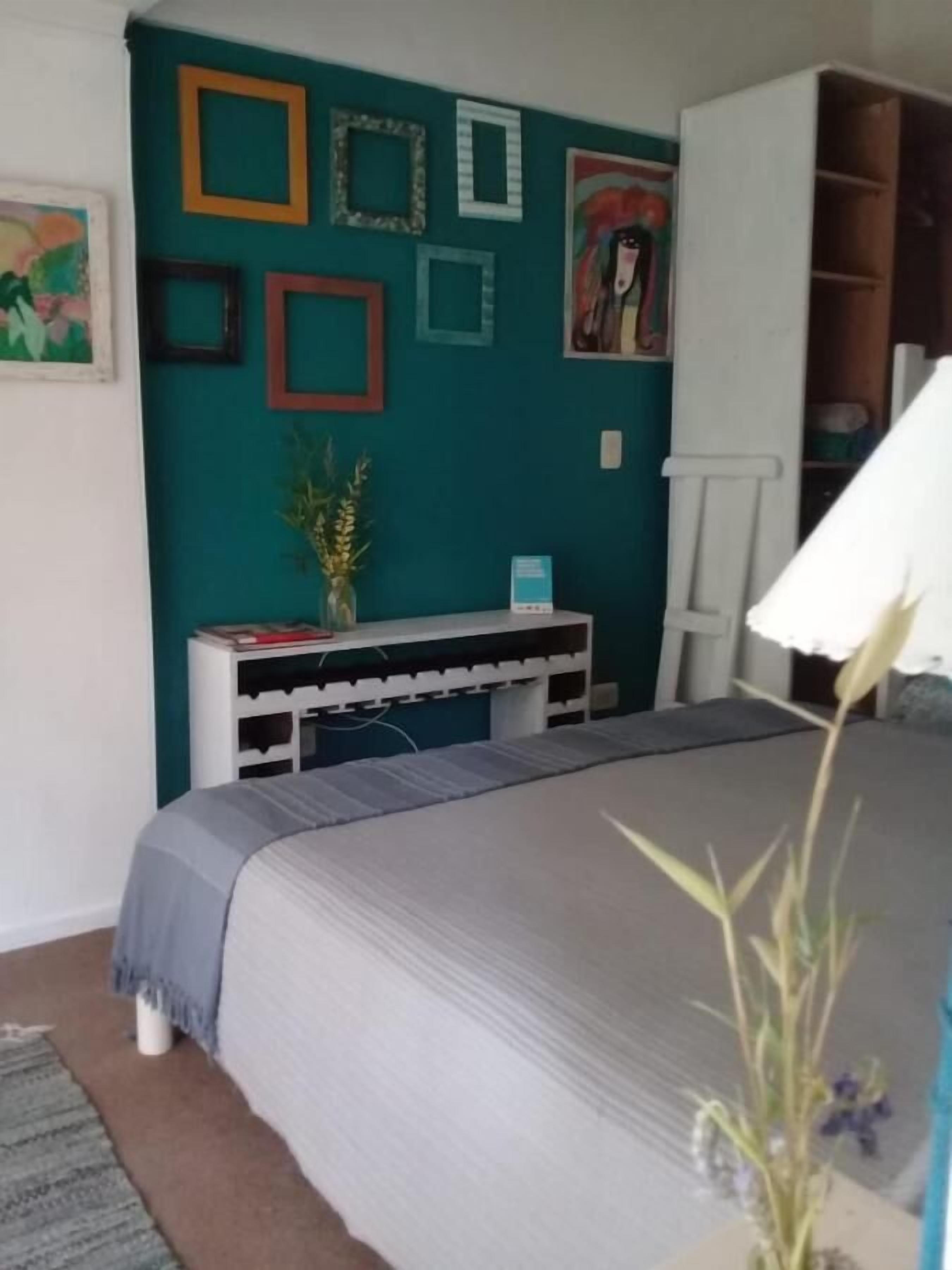 A bedroom with a bed, a white wardrobe, a teal wall, and various framed pictures.