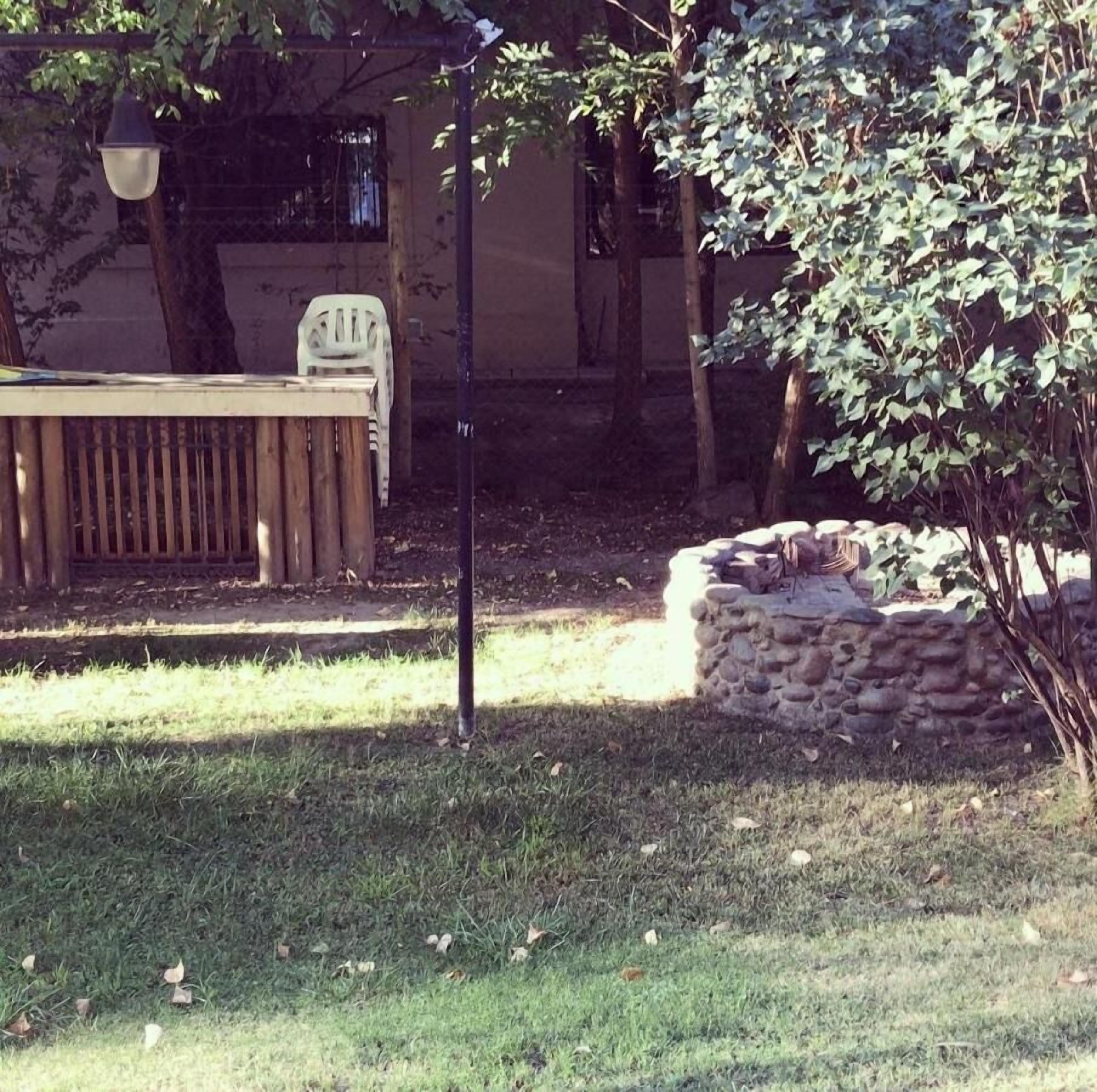 Un'area patio con tavolo e sedie in legno, un muro in pietra e un albero.