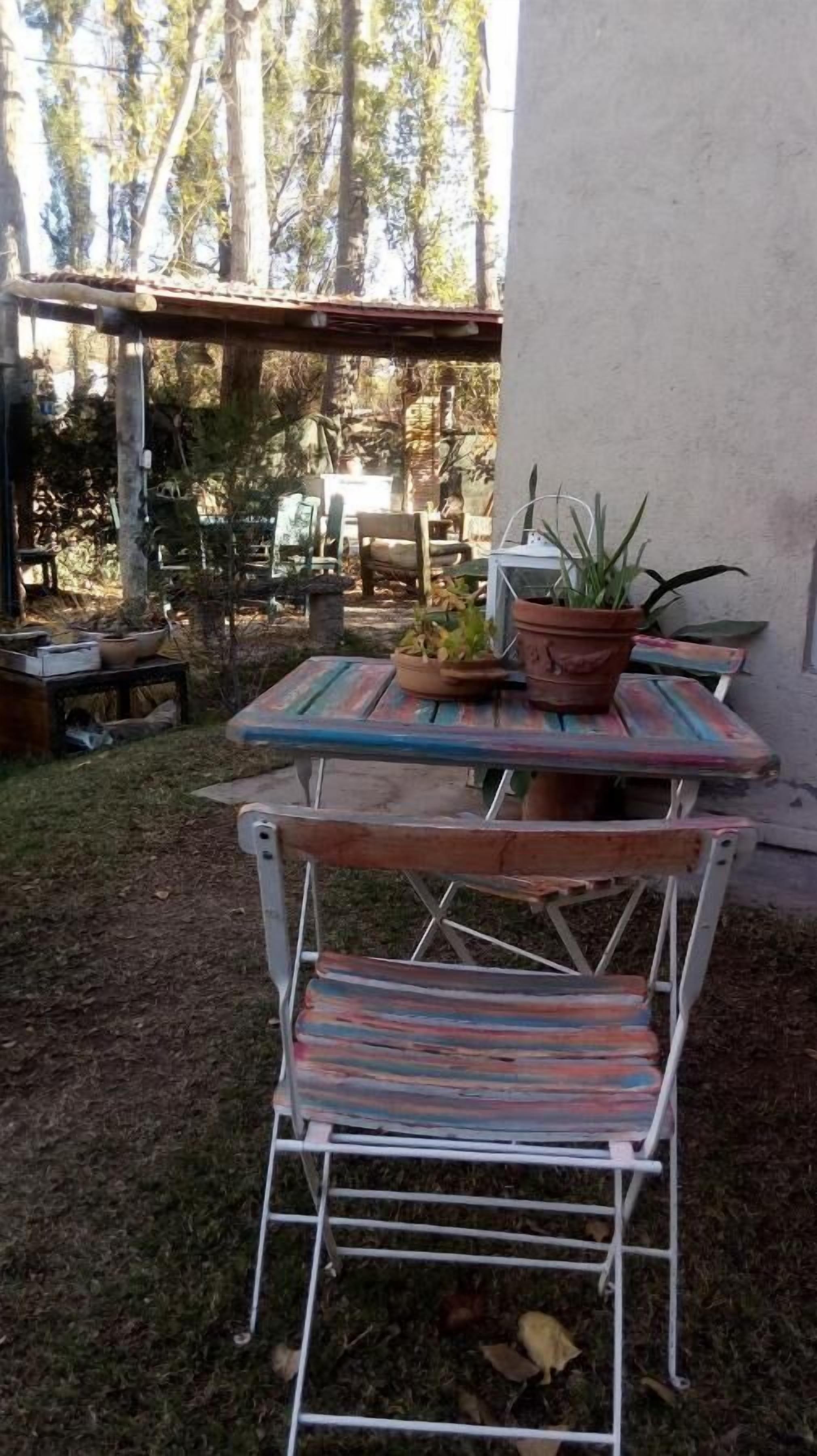 An outdoor patio area with a metal table and chairs, surrounded by potted plants and a stone wall.