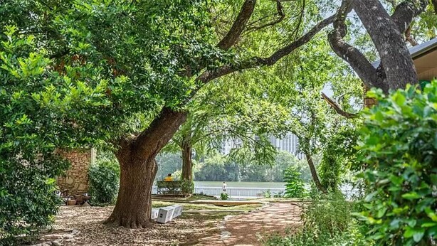 Un jardin avec un mur de pierre, un sentier et une vue sur une étendue d’eau.
