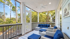 A covered porch with wicker furniture and blue cushions, overlooking a forested area.