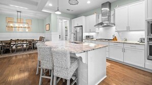 A modern kitchen with white cabinets, a central island with bar stools, a stainless steel range hood, and pendant lighting.