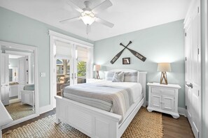 A bedroom with a bed, two bedside tables, a ceiling fan, and a wall-mounted cross.