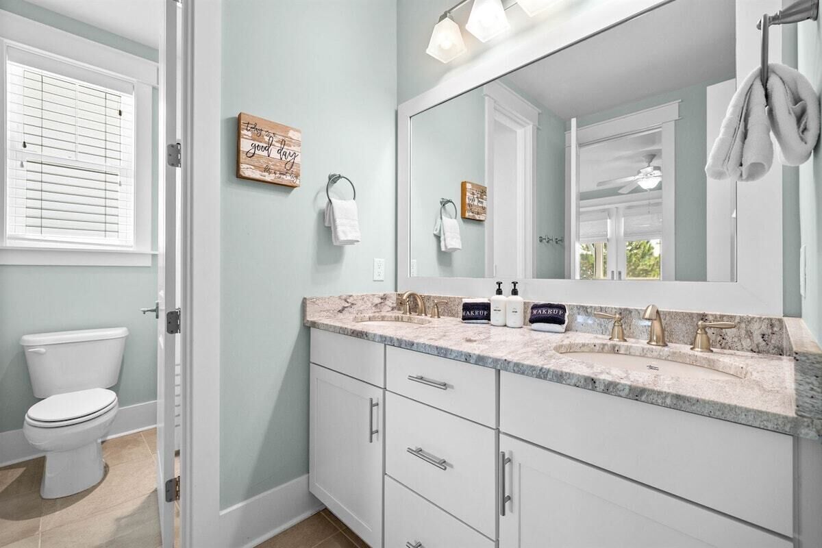 Une salle de bain avec des toilettes blanches, un meuble-lavabo doté d’un plan de travail en marbre et un grand miroir.