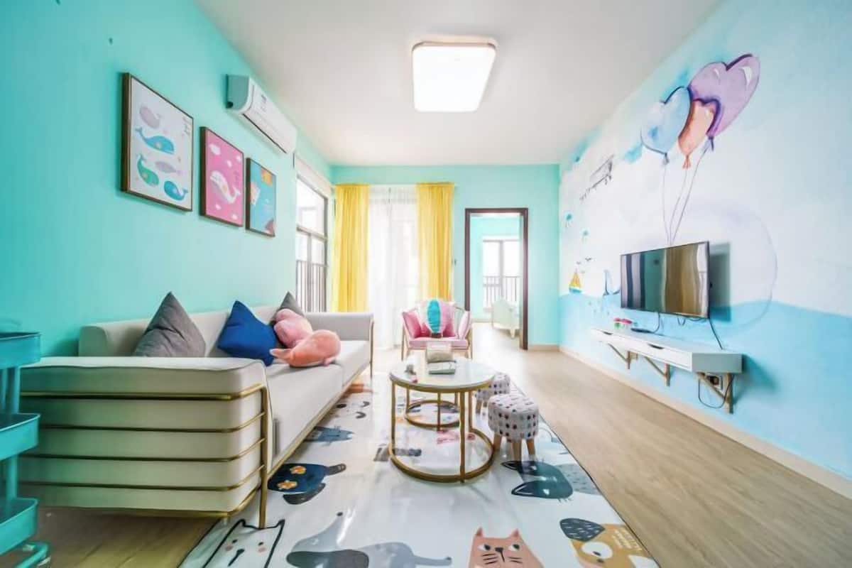 Een woonkamer met een bank, een salontafel en een televisie. Er hangen ingelijste foto’s aan de muur en er is een muurschildering.