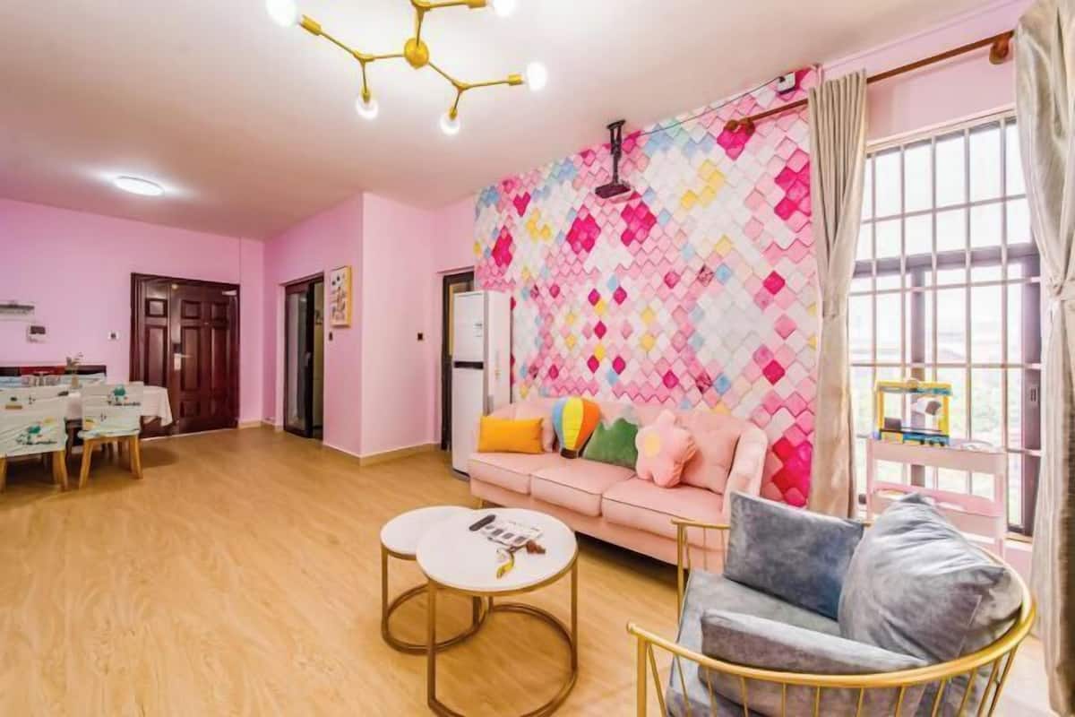 Een woonkamer met een roze muur, een bank, een stoel en een eethoek met een tafel.