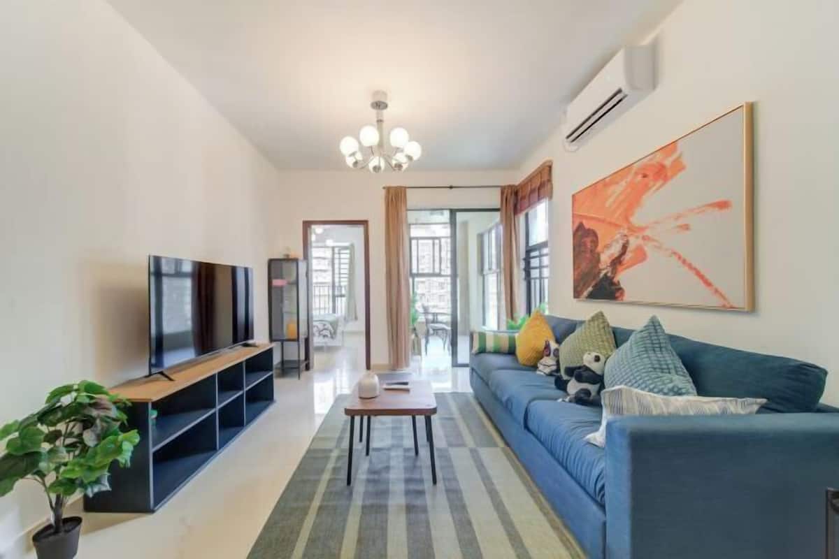 Een moderne woonkamer met een televisie, bank, salontafel en een groot abstract schilderij.
