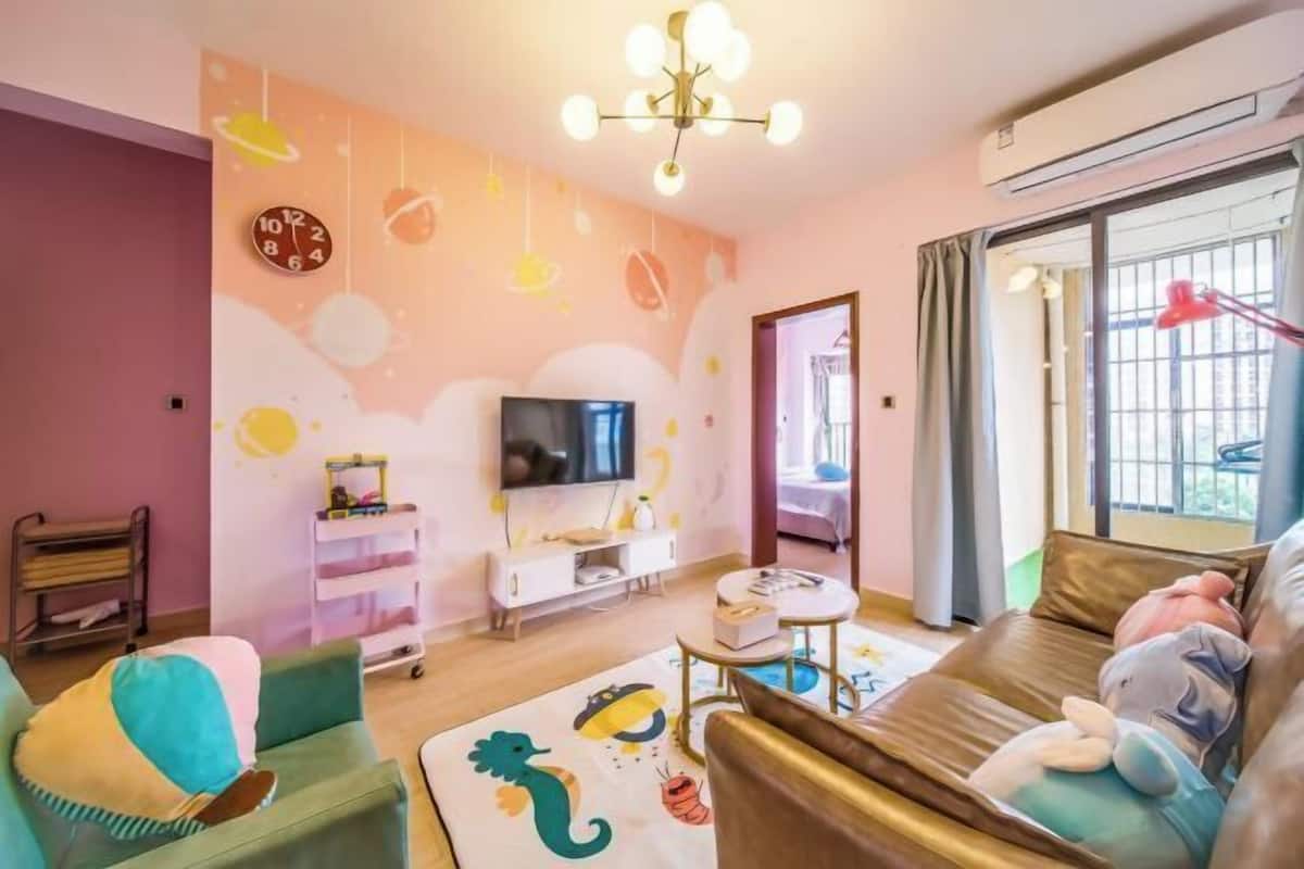 Een gezellige woonkamer met een televisie, bank en kleurrijke wanddecoraties.