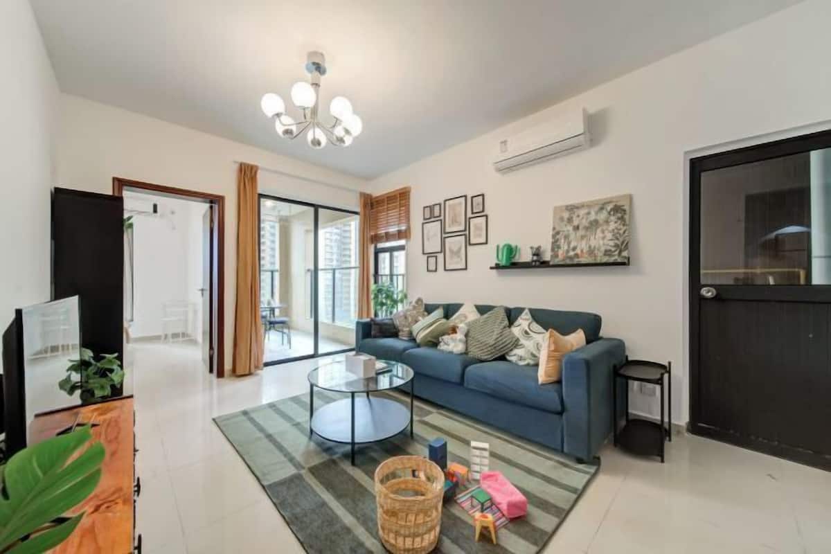 Een moderne woonkamer met een blauwe bank, een glazen salontafel en een groot raam.