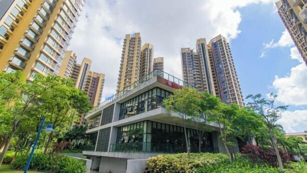Un bâtiment moderne à la façade vitrée, entouré de verdure et bordé d’immeubles résidentiels de grande hauteur.