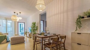 Un coin repas avec une table en bois, des chaises et un lustre. On y trouve également un canapé et un meuble orné de plantes.