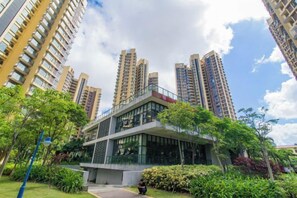 A modern building with a glass facade, surrounded by greenery and adjacent high-rise residential buildings. - Dream House (Zhuhai)