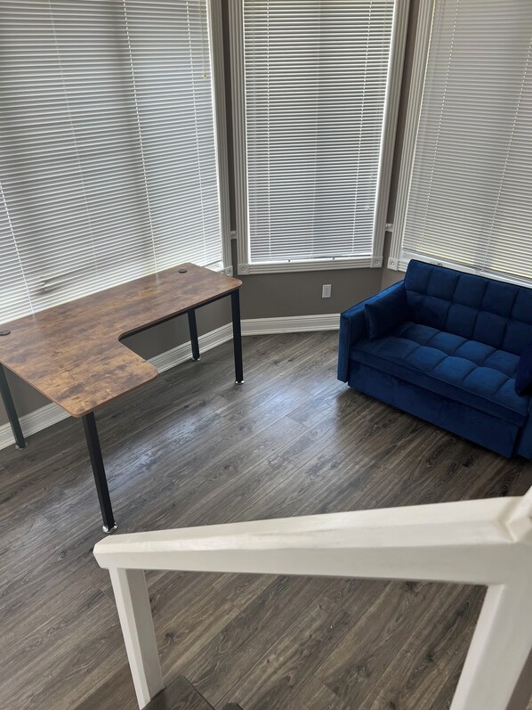 Um quarto com uma mesa de madeira, um sofá azul e janelas amplas com persianas.