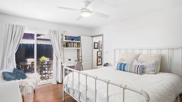 Un dormitorio con cama blanca, ventilador de techo y vistas al exterior.