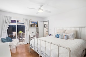 A bedroom with a white bed, a ceiling fan, and a view of the outdoors.