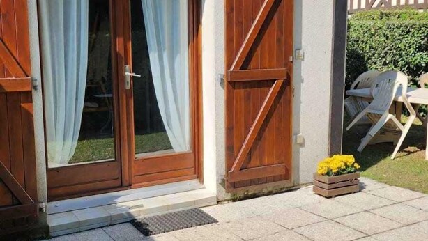 A house with a large sliding glass door, a wooden shutter door, and a small porch area with outdoor furniture.