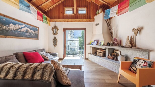 A cozy living room with a wooden ceiling, a sofa with a fur throw, a wooden coffee table, and a colorful flag decoration. - Spacious loft on pedestrian street with views (Chamonix-Mont-Blanc)