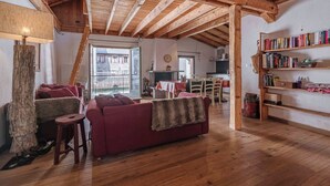 A cozy living room with a wooden ceiling, a red sofa, a wooden bookshelf, and a dining area with a table and chairs. - Spacious loft on pedestrian street with views (Chamonix-Mont-Blanc)