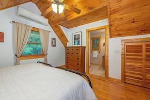 A bedroom with a bed, wooden ceiling, an air conditioning unit, a dresser, and a door leading to another room. - Primrose Cabin | Hot Tub + Fireplace | River Views (Burnsville)