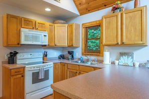 A kitchen with wooden cabinets, a white stove, and a microwave. - Primrose Cabin | Hot Tub + Fireplace | River Views (Burnsville)