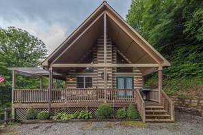 A cabin with a wooden exterior, a porch, and a staircase leading to the entrance.
