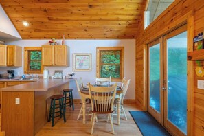 A wooden interior with a kitchen area, dining table, and bar stools. - Primrose Cabin | Hot Tub + Fireplace | River Views (Burnsville)