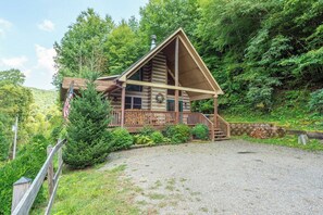 A log cabin with a porch, surrounded by dense forest. - Primrose Cabin | Hot Tub + Fireplace | River Views (Burnsville)