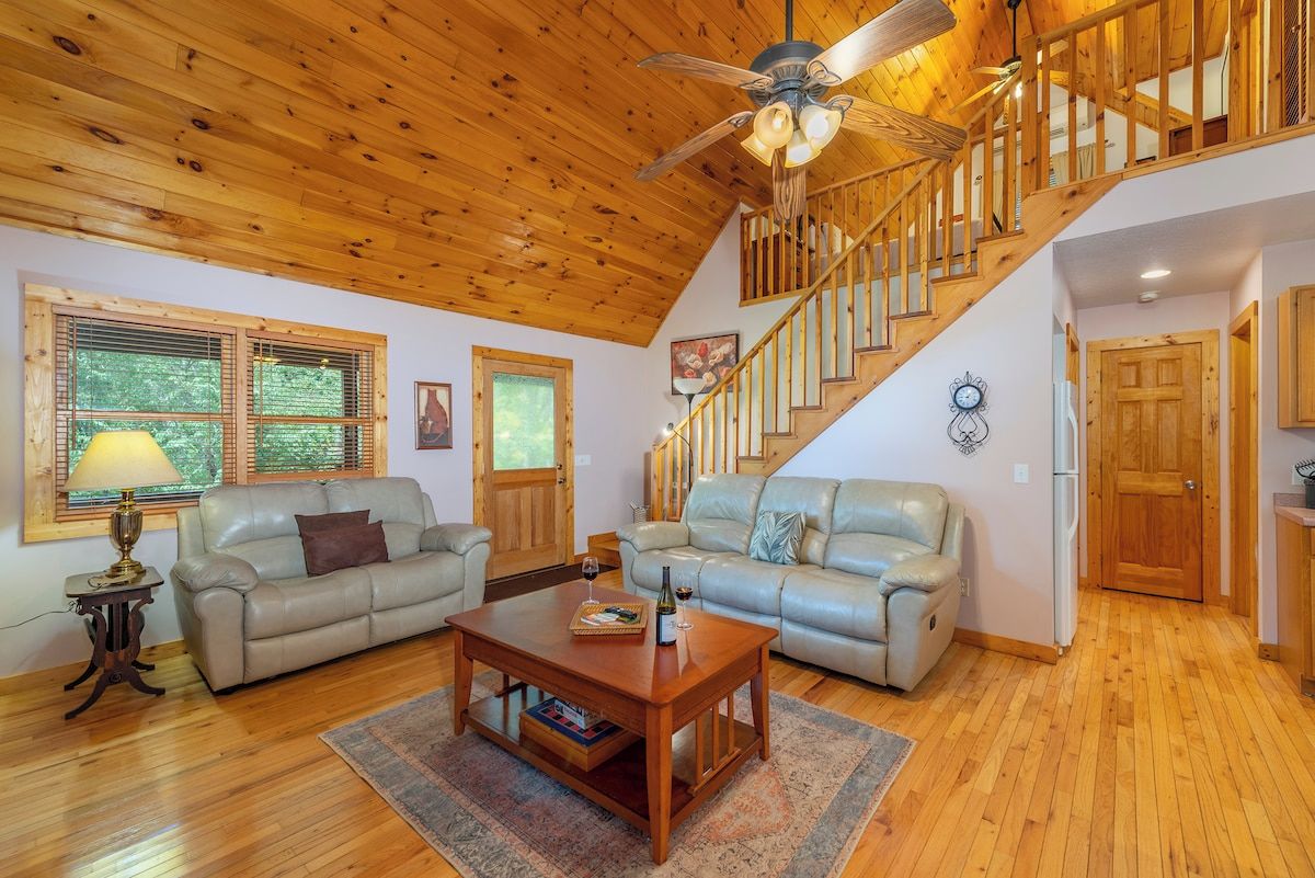 A spacious living room with a wooden ceiling, a staircase, and two leather sofas.