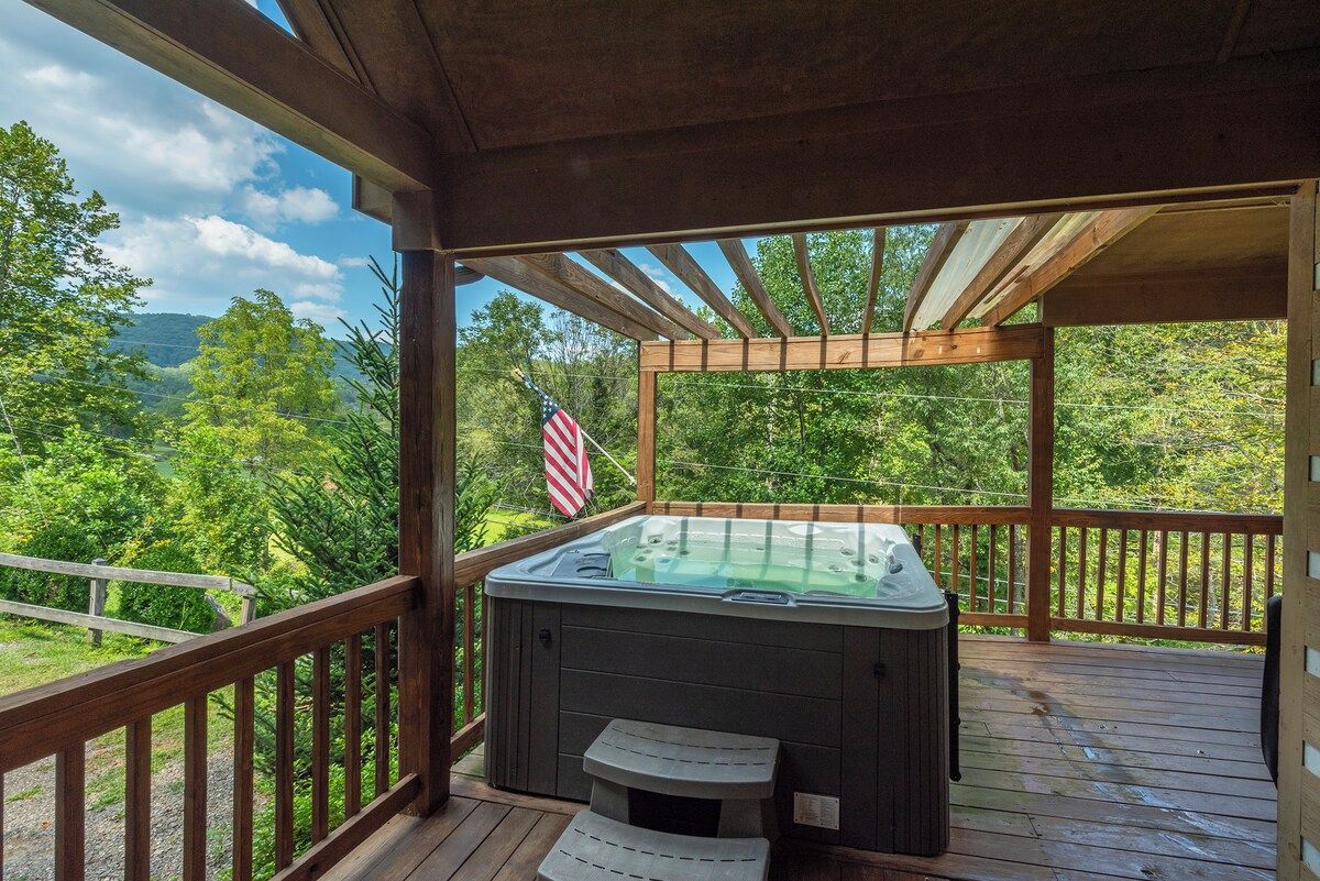 A hot tub on a wooden deck with a view of a forest and mountains.