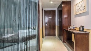 Un couloir d’hôtel avec une cloison en verre, des portes en bois, une petite table avec une bouilloire et un tableau encadré au mur.