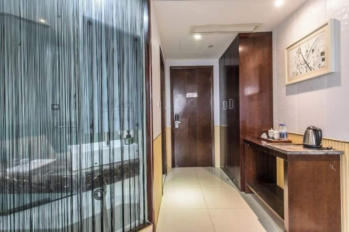 A hotel corridor with a glass partition, wooden doors, a small table with a kettle, and a framed picture on the wall.