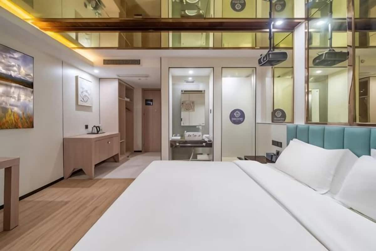 A hotel room with a bed, a vanity, a mirror, and a ceiling with a light fixture.