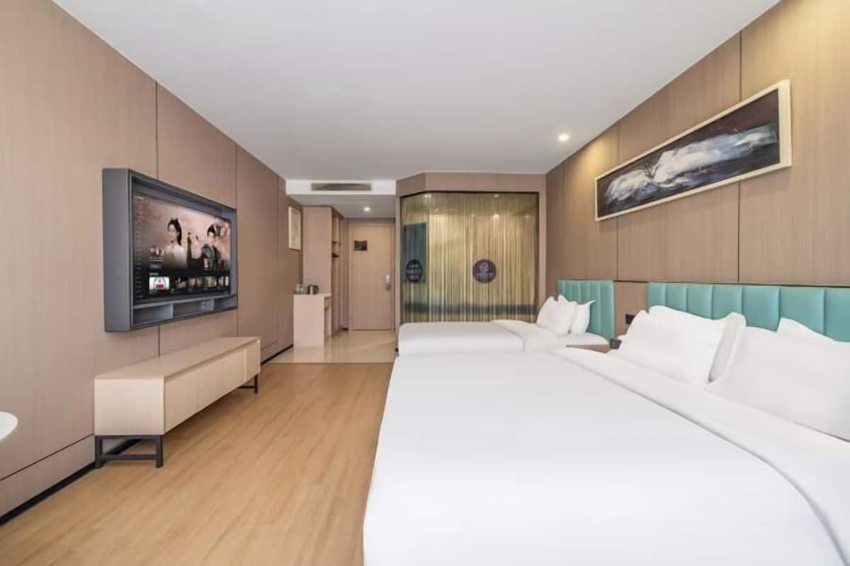 A hotel room with a large bed, a TV mounted on the wall, a bench, and a painting.
