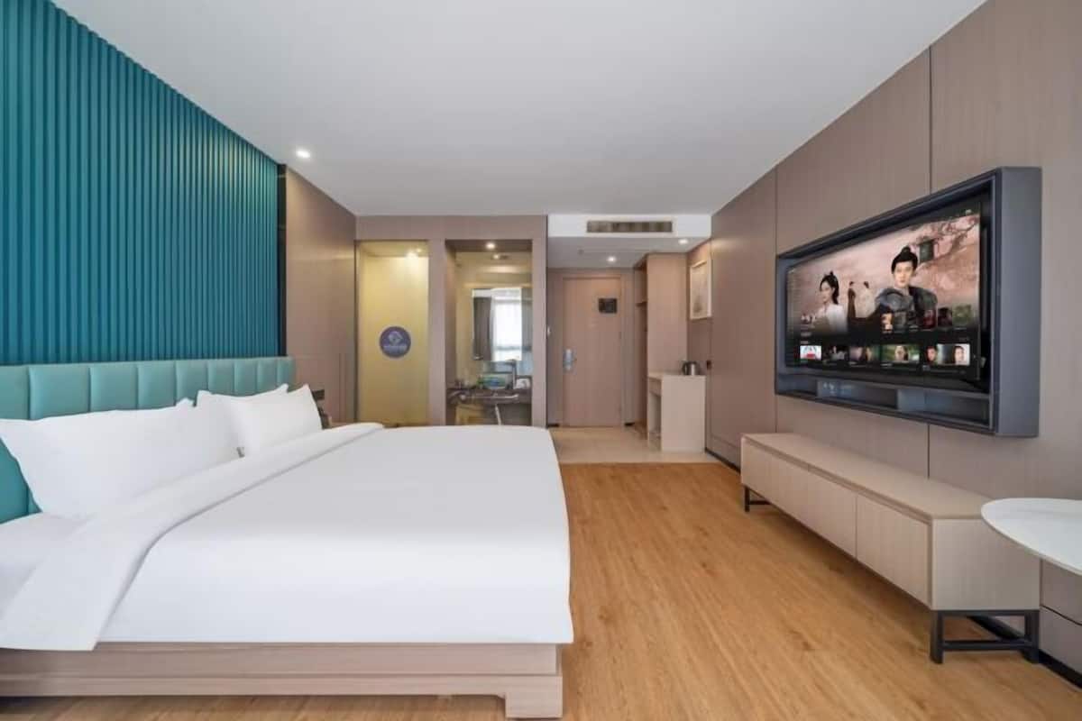 A modern hotel room with a large bed, a TV mounted on the wall, a bench, and a small table.