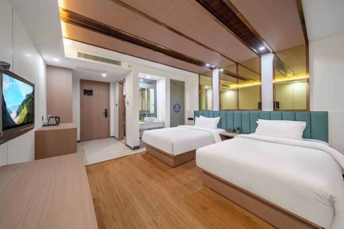 A hotel room with two beds, a TV, a desk, and a mirror.