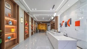 Un hall d’hôtel moderne avec un comptoir d’accueil, des étagères en bois ornées d’objets décoratifs et un mur de marbre agrémenté d’œuvres d’art abstraites.