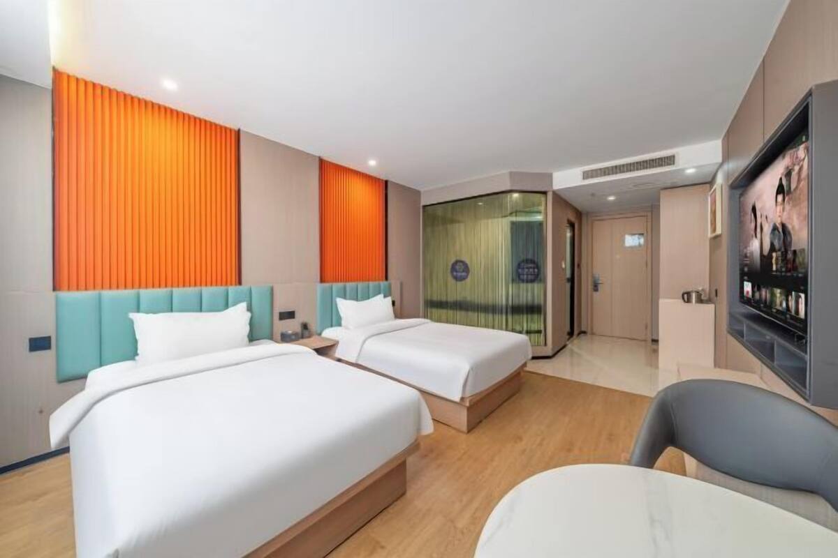 A hotel room with two beds, a TV, a desk, and a bathroom visible through a glass door.