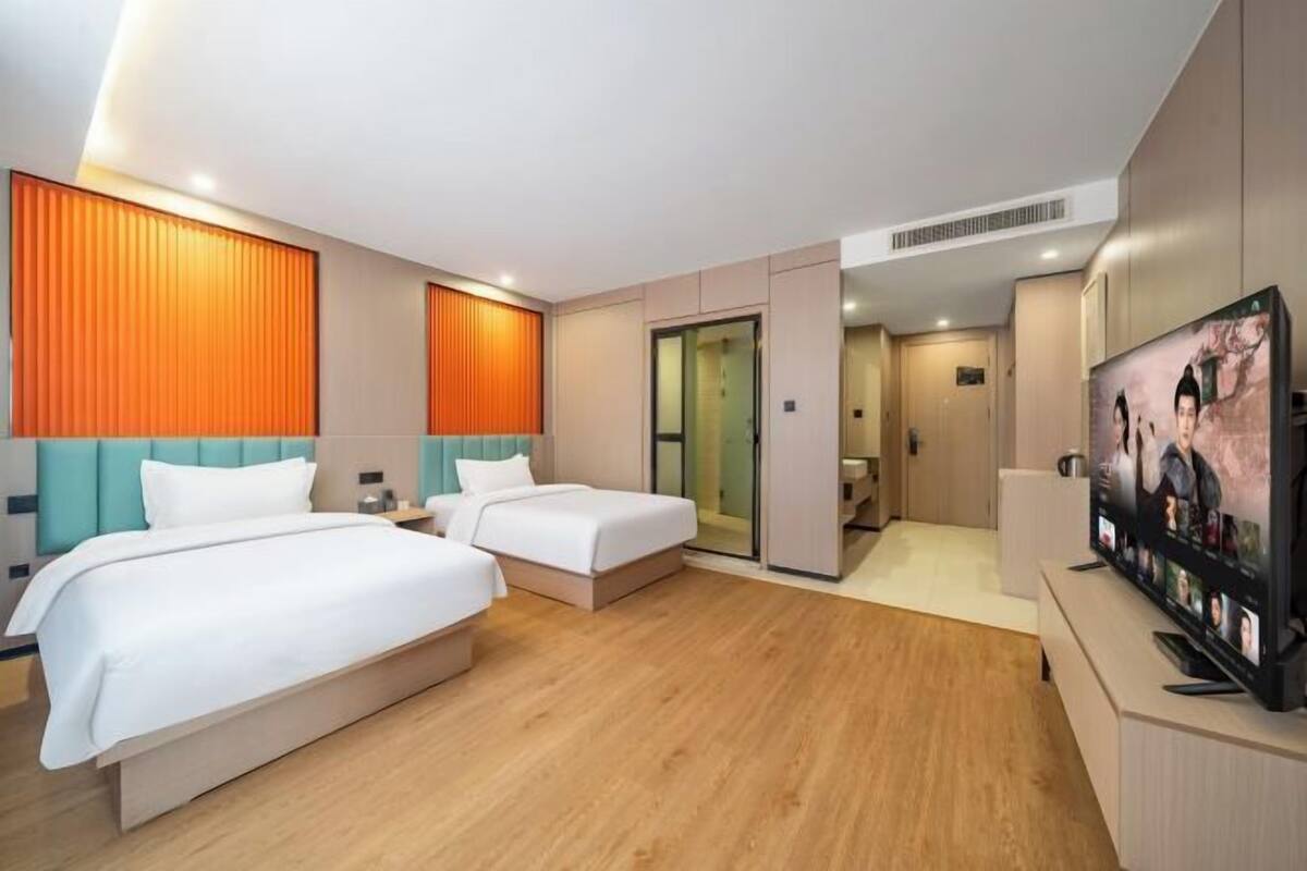A hotel room with two beds, a television, and a bathroom visible through an open door.