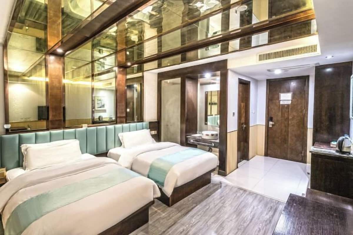 A hotel room with two beds, a large mirror, and a view of the city through a glass wall.