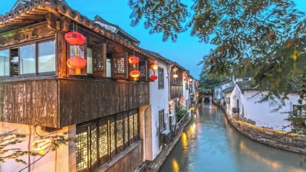 Un bâtiment traditionnel en bois, avec un étroit canal devant, illuminé par des lanternes suspendues.