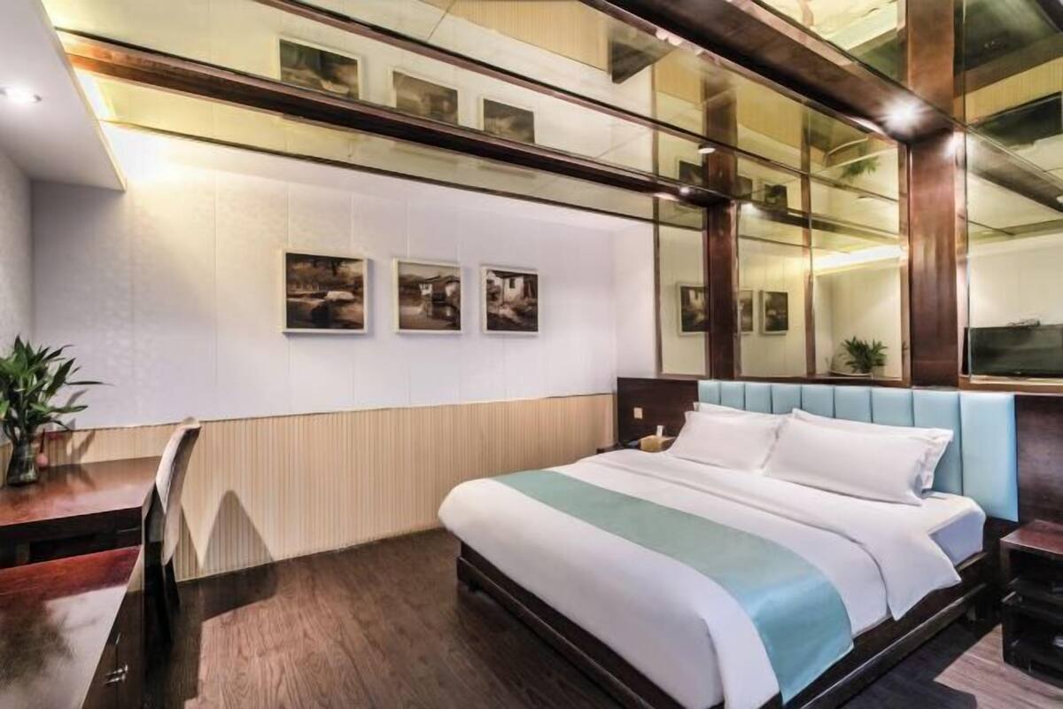 A hotel room with a large bed, a wooden headboard, a small bedside table, a mirror, and a wall with framed pictures.