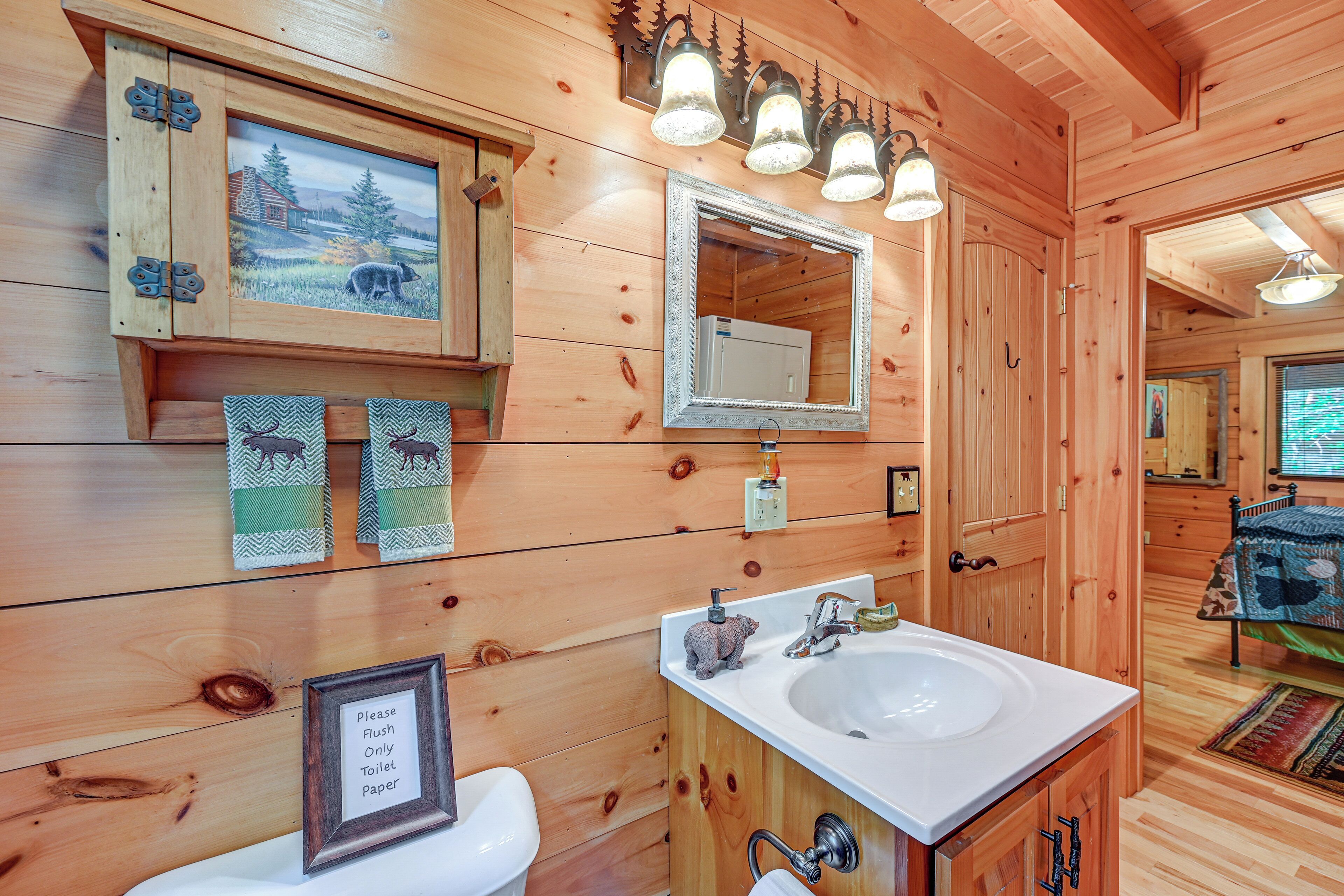 A wooden cabin bathroom with a sink, mirror, and a framed picture of a cabin on the wall.