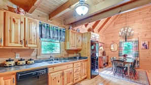 A wooden cabin with a kitchen featuring wooden cabinets, a dishwasher, a refrigerator, and a dining area with a table and chairs. - Serene Cabin < 1 Mi to Fairy Stone State Park! (Stuart)