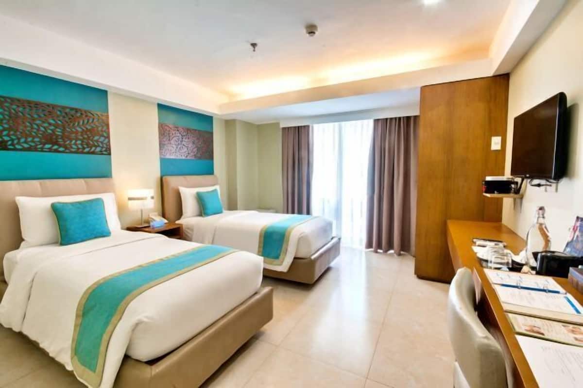 Une chambre d’hôtel avec deux lits, un bureau, un téléviseur à écran plat et une grande fenêtre avec des rideaux.