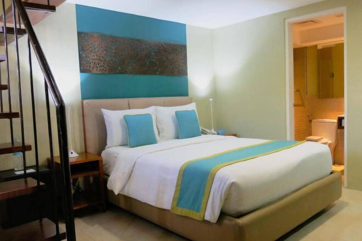 Une chambre à coucher avec un lit, des tables de chevet, une lampe, un escalier et une salle de bain visible à travers une porte ouverte.