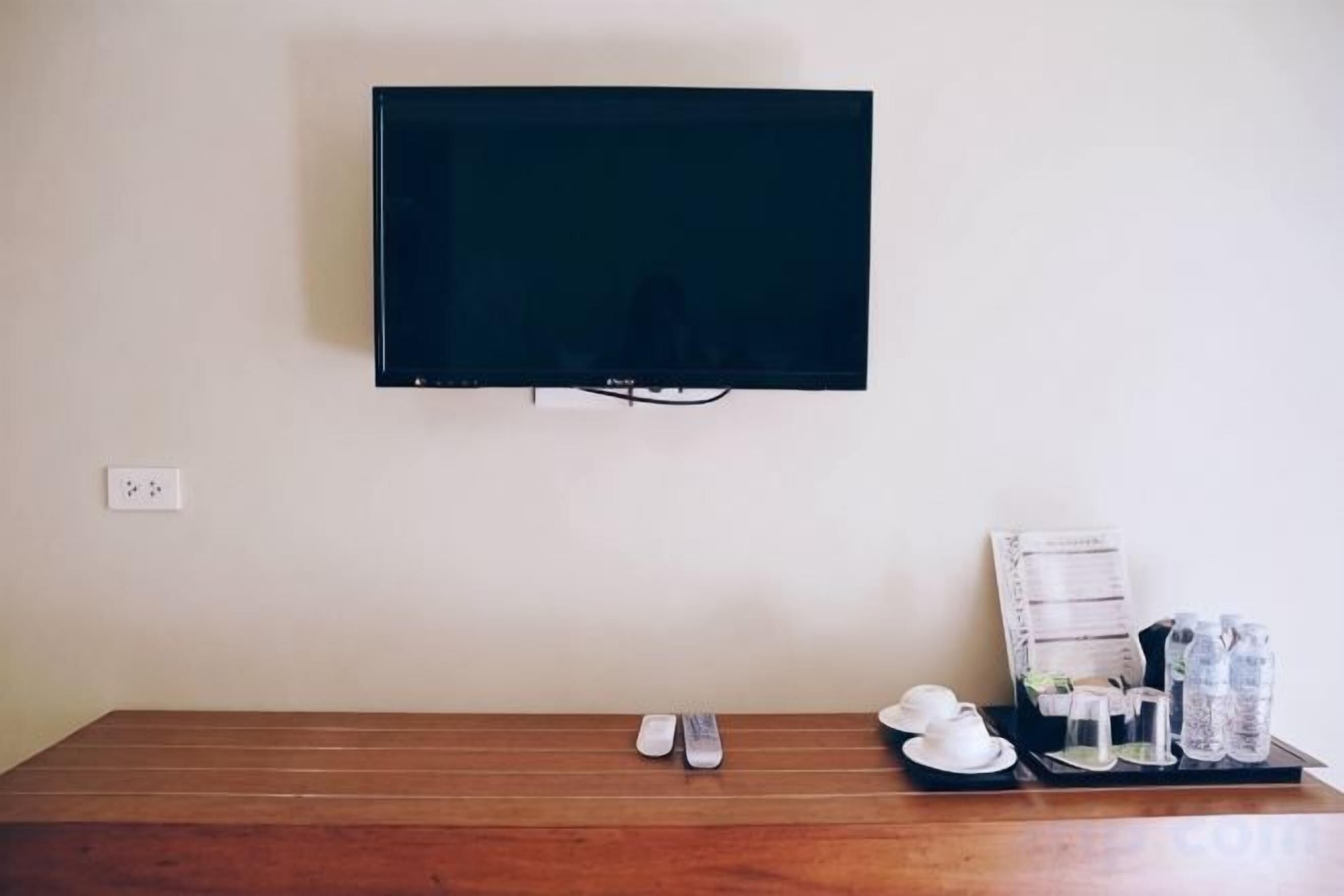 Una habitación con un televisor de pantalla plana montado en la pared, una mesa de madera con una bandeja que contiene un control remoto, vasos y una botella de agua.