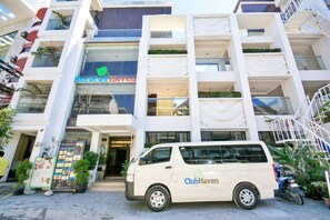 Un edificio de varios pisos con el letrero Club Haven, una camioneta blanca estacionada en la parte delantera y una escalera a la derecha.