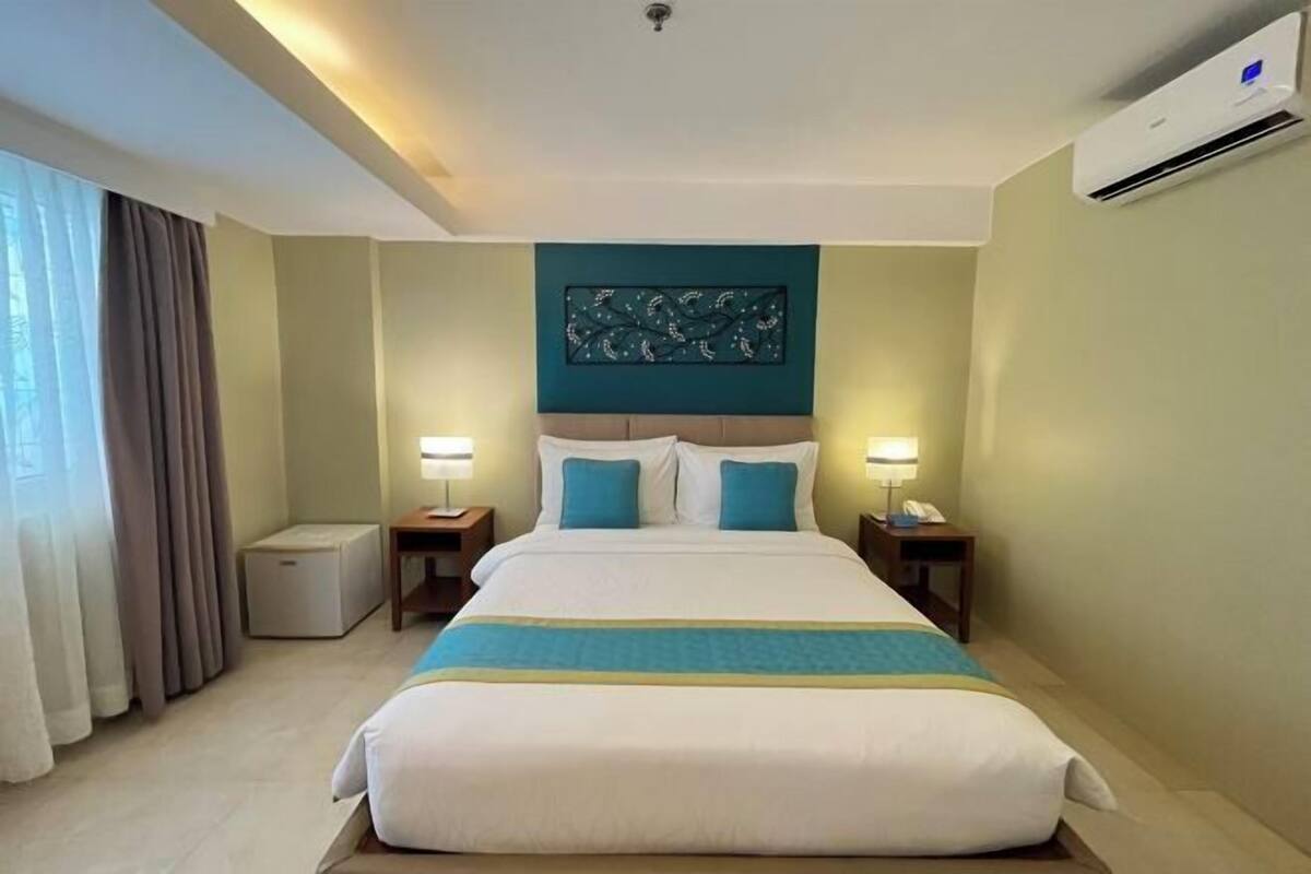 Une chambre d’hôtel avec un lit, deux tables de chevet, un climatiseur fixé au mur et une fenêtre avec des rideaux.