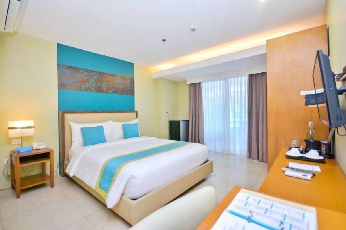 Une chambre d’hôtel avec un lit, un bureau avec un ordinateur, un téléphone et une fenêtre avec des rideaux.