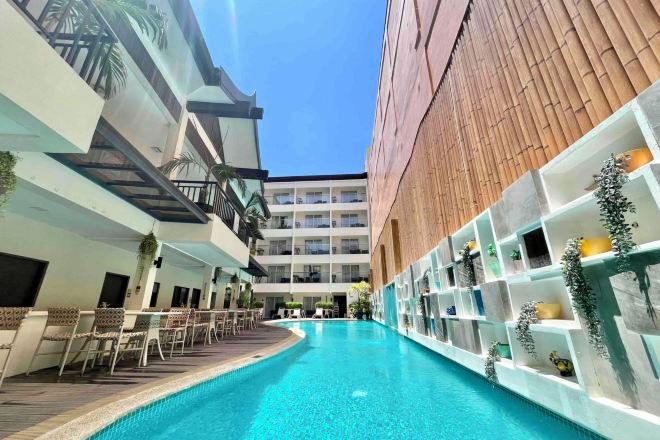 A modern hotel with a central swimming pool, outdoor seating, and a multi-level building with balconies.